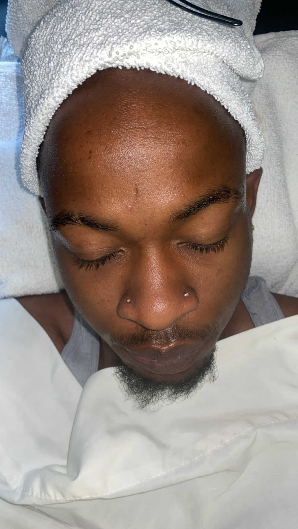 Client resting during a men's signature facial with a warm towel wrap